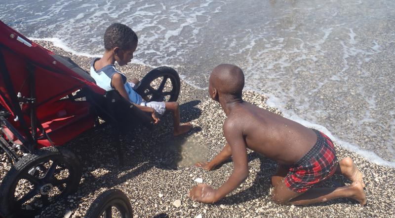 Malachi, right, who cannot walk or stand on his own, is given a small puddle of water by  his house brother so he too can experience the water.